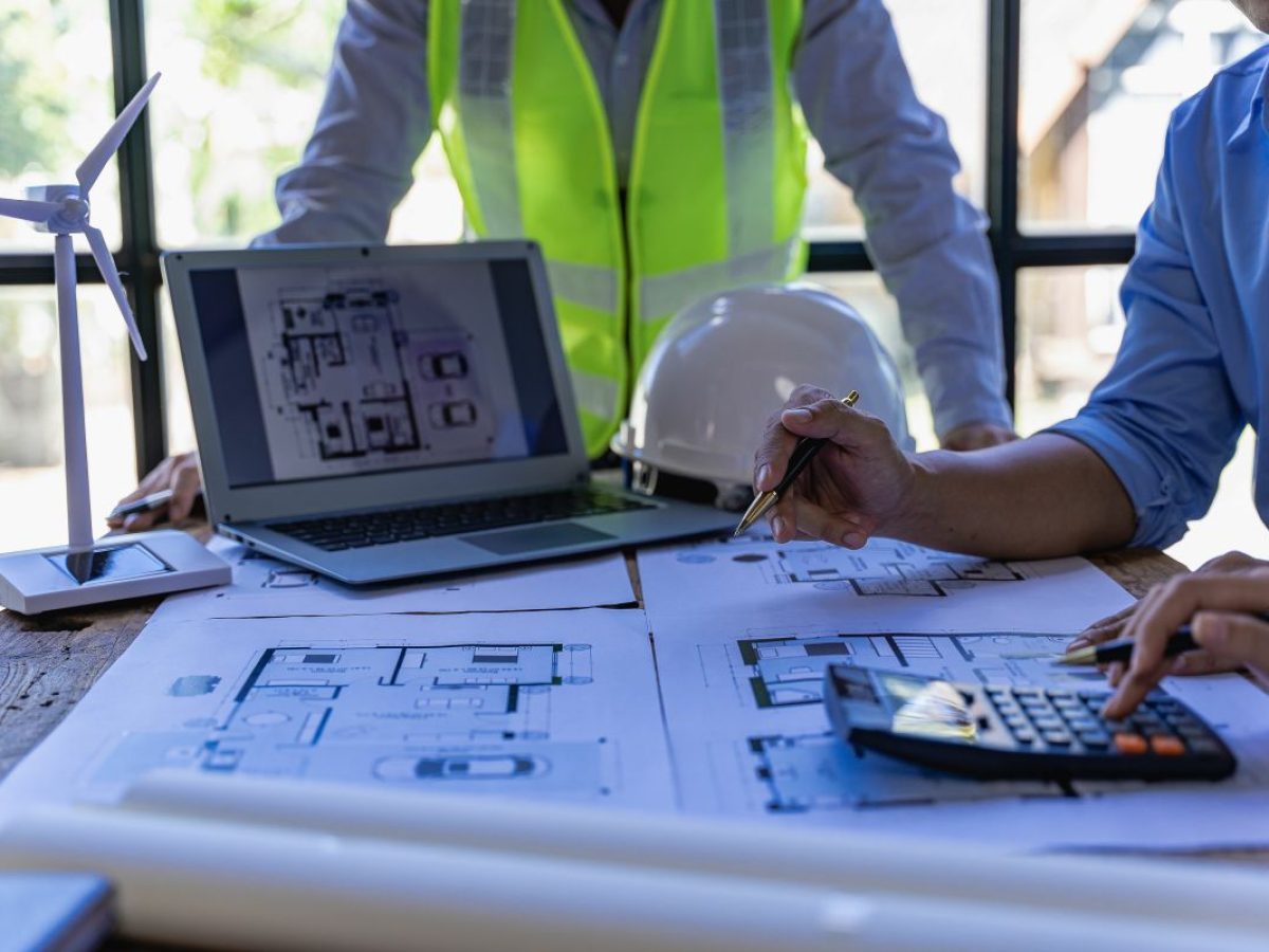 Arquitetos e engenheiros apontam para edifícios em plantas e usam laptops para desenhar projetos de casas em um escritório de conceito de construção